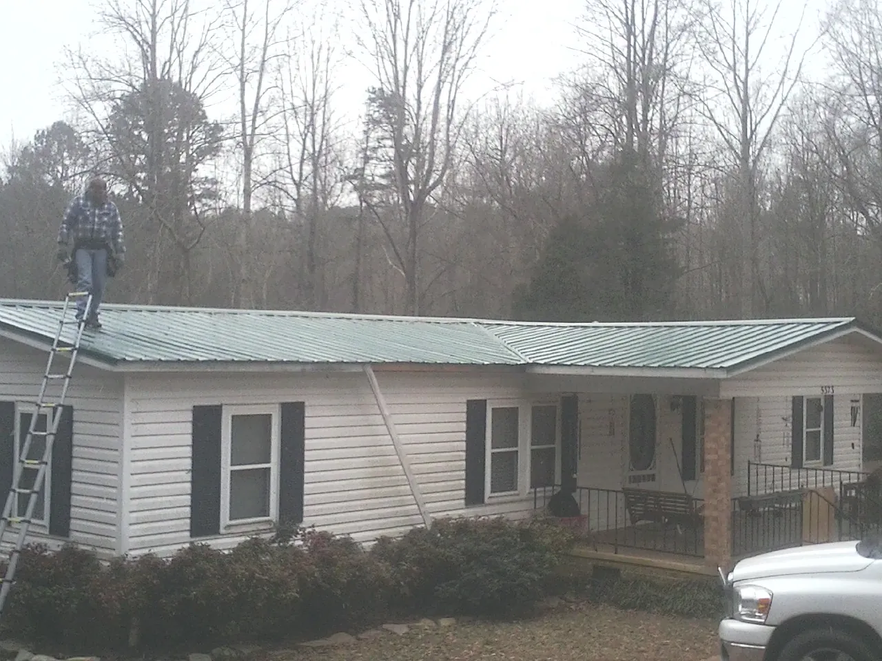 Worker on a ladder beside a new green metal roof on a ranch home in Hamilton